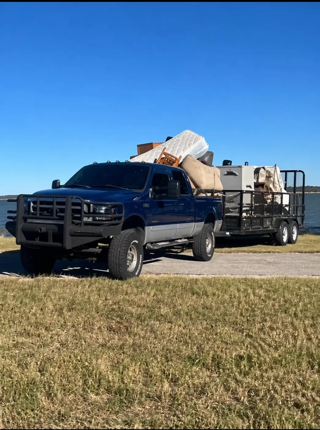 Pickup truck and trailer loaded with a mattress, dresser, couch, and window AC unit for hauling in Oxford, MS